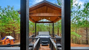 A wooden deck leading to a hot tub with a view of a forest. - Moonshine Times - great outdoor space, hot tub, playground, firepit (Broken Bow)
