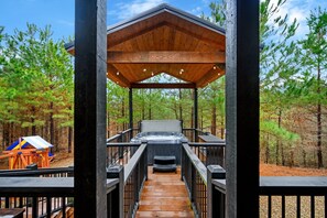 Una terraza de madera que conduce a un jacuzzi con vistas a un bosque.
