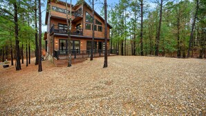 A two-story log cabin with a balcony, surrounded by a forest. - Moonshine Times - great outdoor space, hot tub, playground, firepit (Broken Bow)
