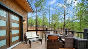 A wooden deck with outdoor furniture and a view of trees. - Moonshine Times - great outdoor space, hot tub, playground, firepit (Broken Bow)