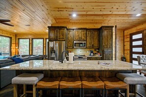 A spacious kitchen with wooden cabinets, a large island with bar stools, and a built-in microwave. - Moonshine Times - great outdoor space, hot tub, playground, firepit (Broken Bow)