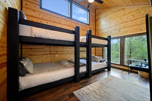 A cabin with three bunk beds, wooden walls, large windows, and a ceiling fan.
