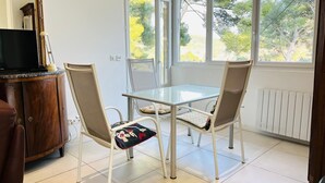 Un comedor con mesa de vidrio y dos sillas, un aparador de madera y vistas a árboles a través de amplios ventanales.