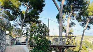 Un sendero pavimentado que conduce a una terraza de madera rústica con asientos exteriores, rodeada de exuberante follaje y árboles.