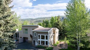 A two-story house with a large front yard, a garage, and a view of hills in the background. - Spacious Home Base! Hot Tub, Fire Pit, Sleeps 10 (Avon)