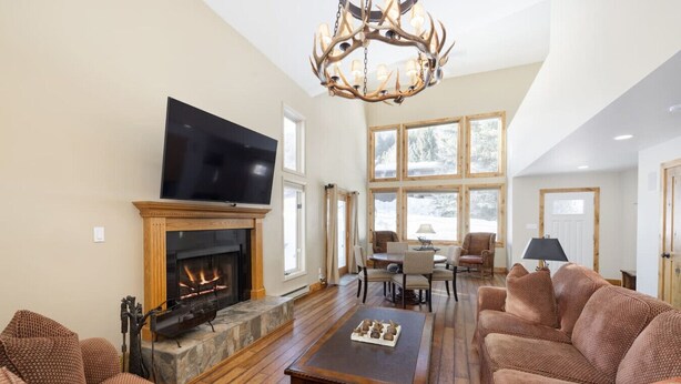 A spacious living room with a fireplace, a large flat-screen TV, and a chandelier. - Spacious Home Base! Hot Tub, Fire Pit, Sleeps 10 (Avon)