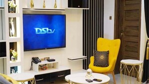 Una sala de estar moderna con un televisor de pantalla plana, un sillón amarillo, una mesita redonda y un sofá.
