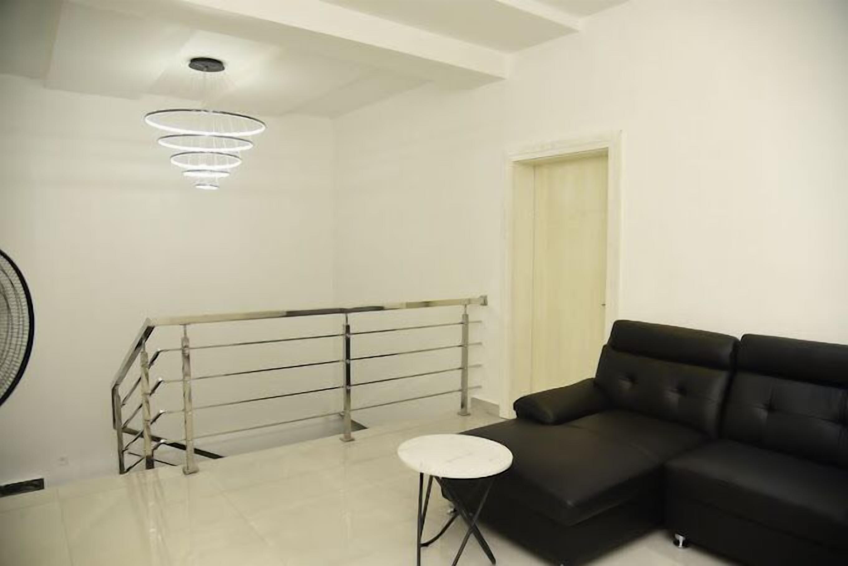 A modern living room with a black sofa, a small white table, a staircase with a metal railing, and a ceiling light fixture.