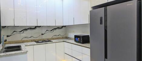 A modern kitchen with white cabinets, a black refrigerator, and under-cabinet lighting.