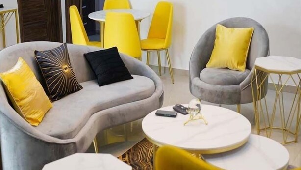 Una sala de estar moderna con un sofá gris, sillones amarillos y una mesa de centro redonda.