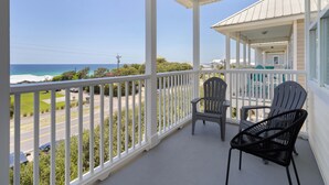 A covered balcony with white railings, two Adirondack chairs, and a view of the ocean.