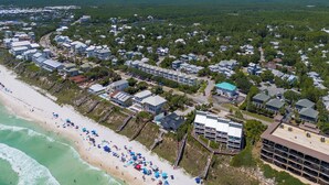 An aerial view of a coastal residential area with beachfront properties, a beach with umbrellas, and a large building with a blue roof.