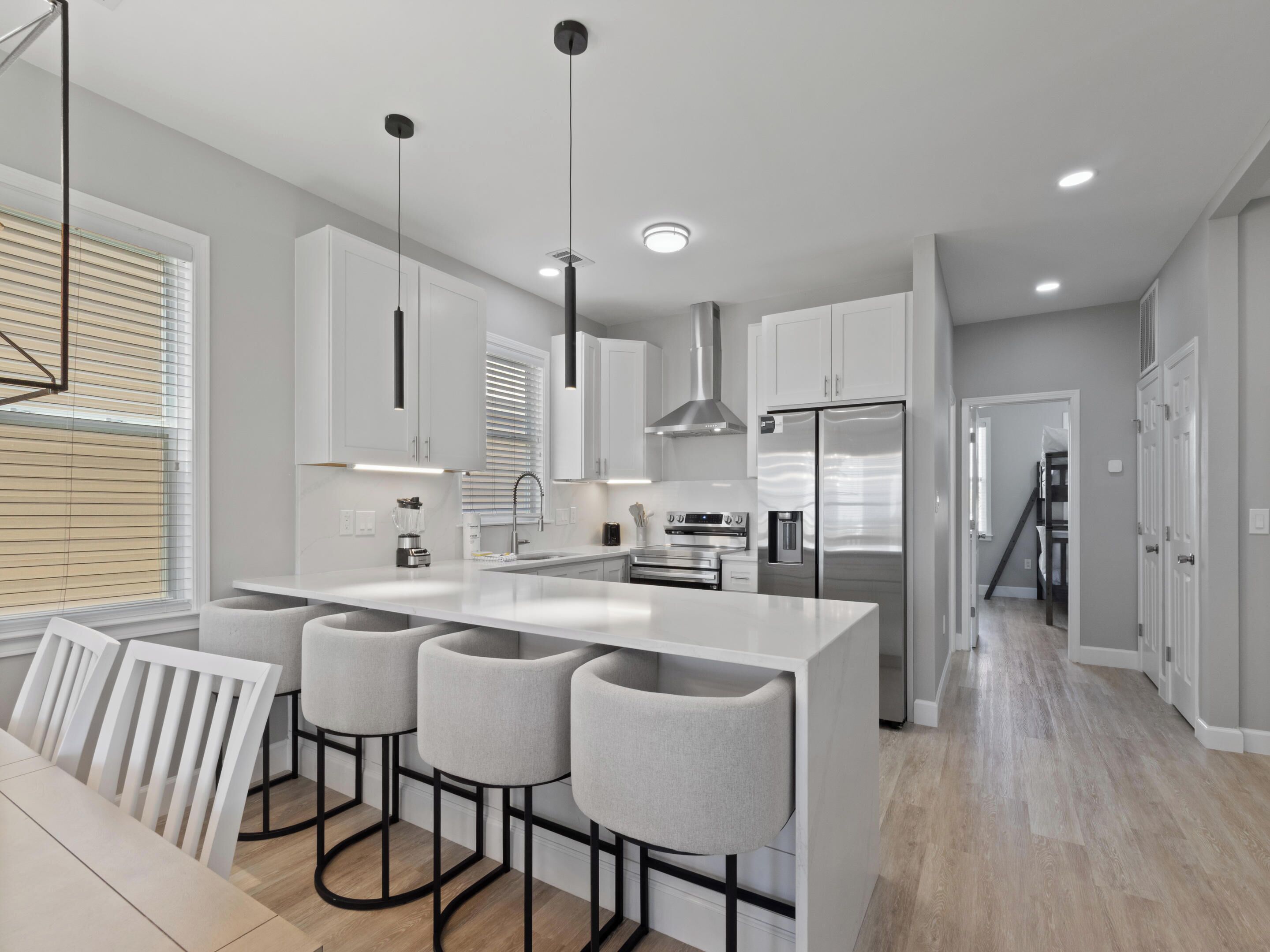 A modern kitchen with a central island, bar stools, stainless steel appliances, and a staircase leading to an upper level.