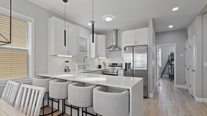 A modern kitchen with a central island, bar stools, stainless steel appliances, and a staircase leading to an upper level.