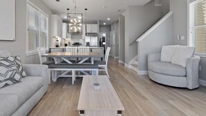 A modern living room with a dining area, a sofa, a coffee table, and a staircase.