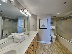 A modern bathroom with a large mirror, dual sinks, a shower enclosure, and framed wall art. - The Beach Club - Avalon #1604 | Luxury Resort w. Pools, Pickleball, Gym + More (Fort Morgan)