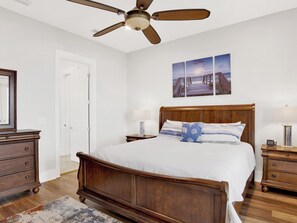 Un dormitorio con cama de madera, dos mesitas de noche con lámparas, un ventilador de techo y una puerta.