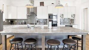 Une cuisine moderne dotée d’un grand îlot central, d’appareils électroménagers en acier inoxydable et de luminaires suspendus.