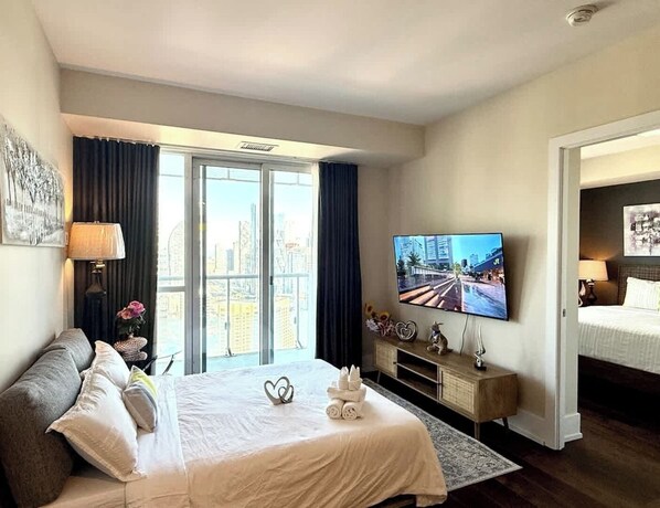 Een hotelkamer met een groot bed, een televisie, een bureau en uitzicht op de stad door de ramen.