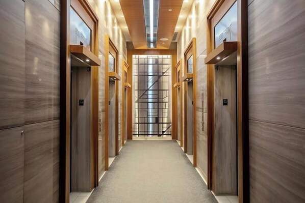 A modern elevator lobby with a central staircase, wooden paneling, and a glass elevator door. - Rogers Center MTCC 2BR/2BA Lake&CN Tower View King Bed  Free Parking (Toronto)