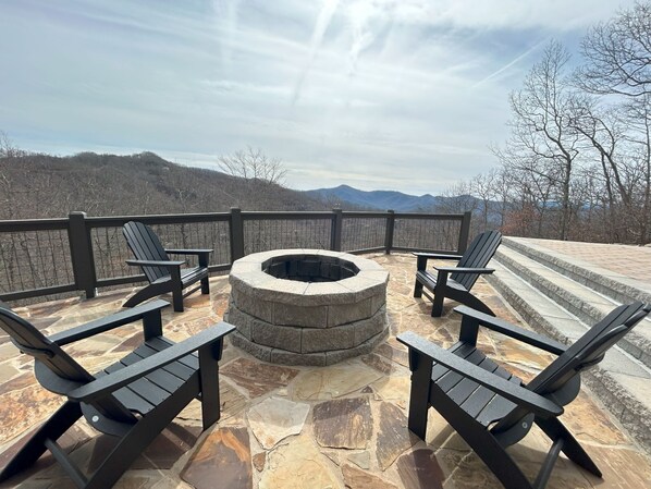 A stone patio with Adirondack chairs and a fire pit, overlooking a mountainous landscape.
