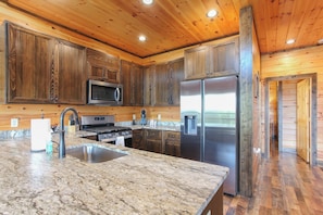 A kitchen with wooden cabinets, a stainless steel refrigerator, a microwave, and a granite countertop.