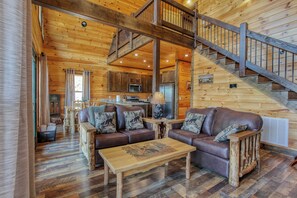 A log cabin interior with a wooden staircase, a dining area, and a kitchen.