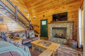 Ein Blockhaus-Interieur mit Kamin aus Stein, Ledersofa, Couchtisch aus Holz und einer Treppe.