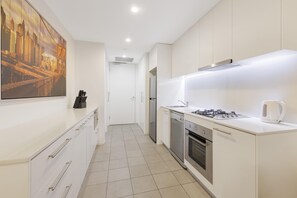 A modern kitchen with white cabinetry, a stainless steel refrigerator, a gas stove, and a kettle. - Oaks Melbourne Flemington Suites (Travancore)
