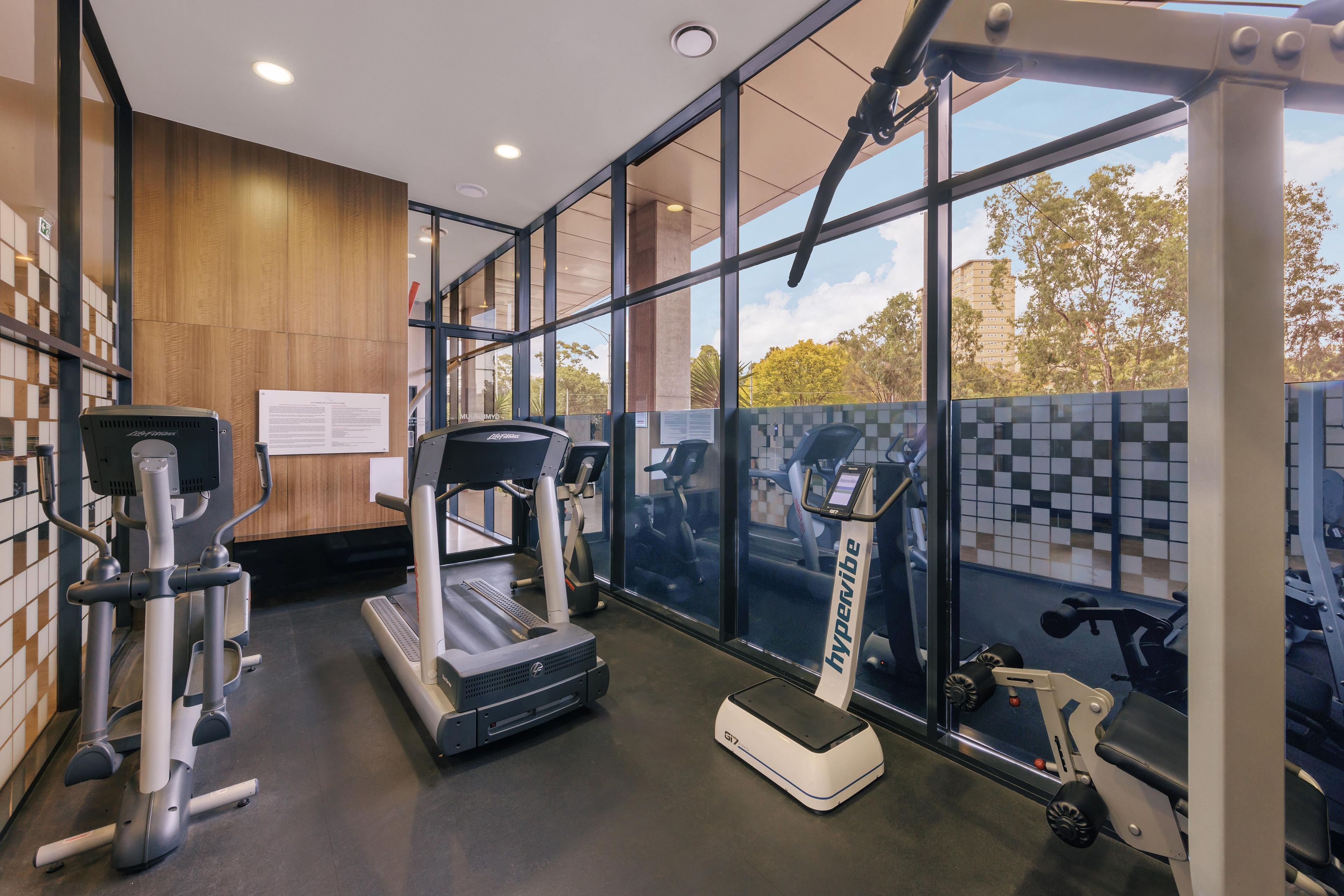 Un gimnasio con máquinas de cardio, equipo de pesas y amplias ventanas con vistas al exterior.