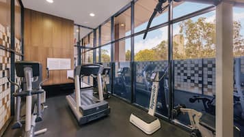 A gym with cardio machines, weight equipment, and large windows offering a view of the outdoors.