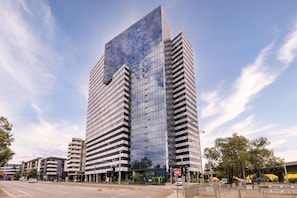 A modern high-rise building with a glass facade, surrounded by a cityscape. - Oaks Melbourne Flemington Suites (Travancore)