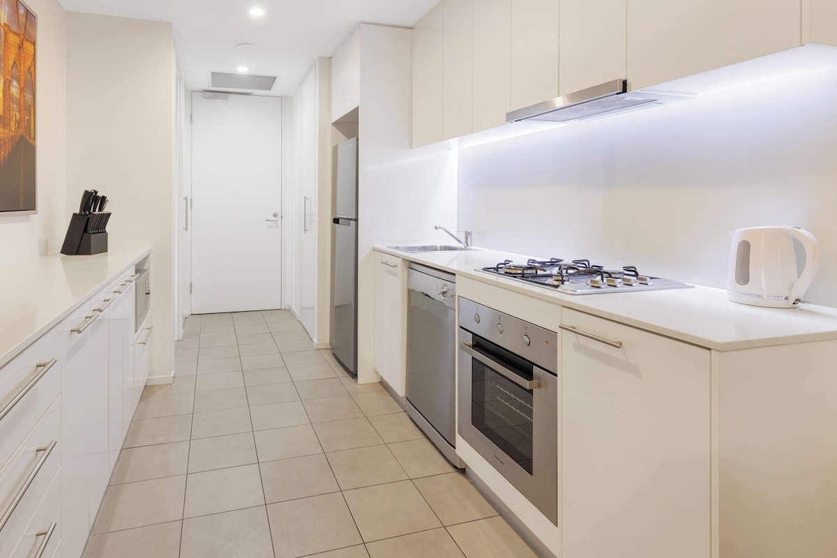 Una cocina moderna con armarios blancos, electrodomésticos de acero inoxidable y piso de baldosas.