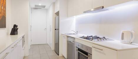 A modern kitchen with white cabinetry, stainless steel appliances, and a tiled floor.