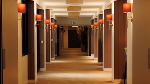 Een hotelgang met houten vloeren, wandlampen en deuren aan beide zijden.