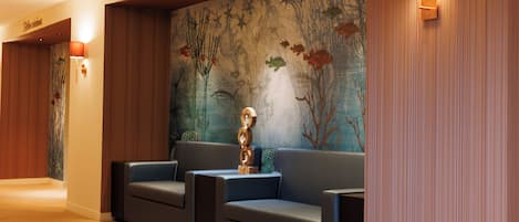 A modern lobby with a wooden floor, a blue sofa, and a mural with plant and tree designs.