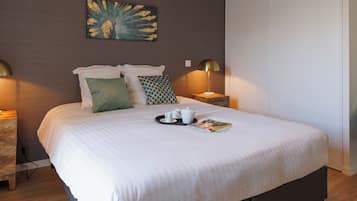 Een net opgemaakt bed met een dienblad thee, een tijdschrift, twee bedlampjes en een kunstwerk aan de muur.