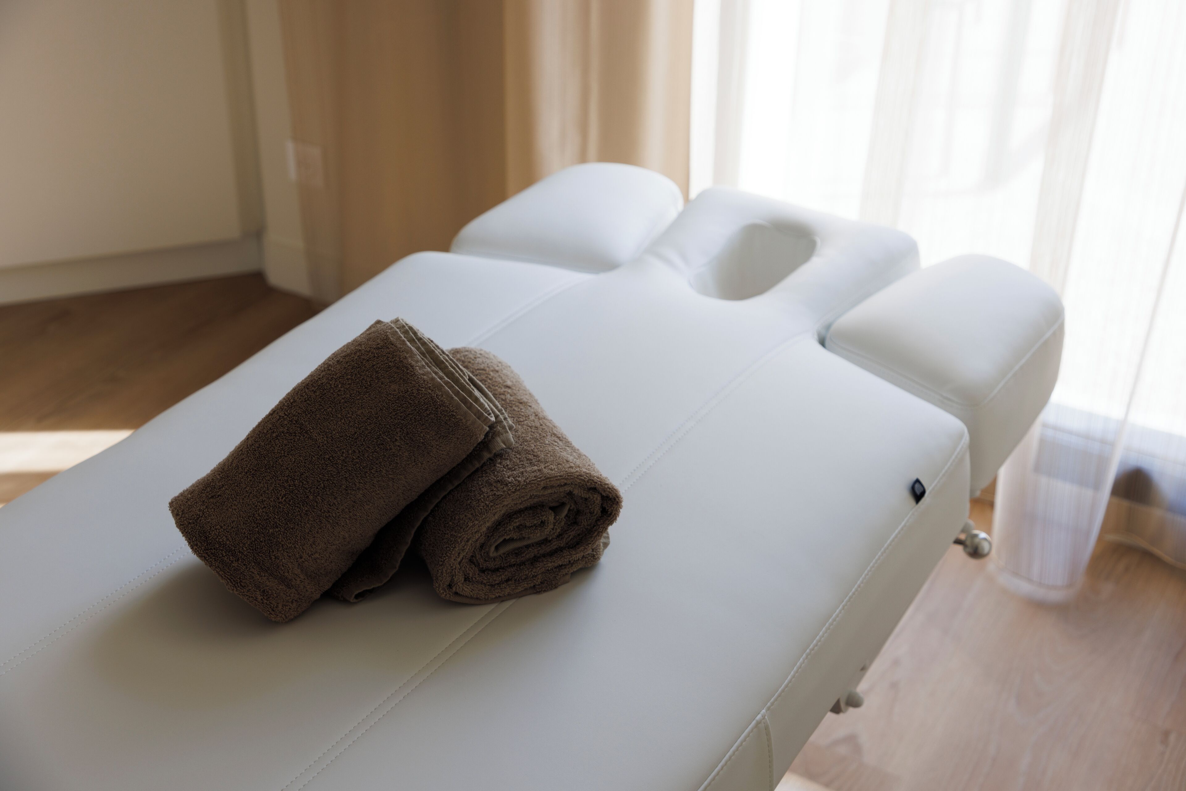 Ett massagebord med handdukar, ett vitt nackstöd och ett trägolv.