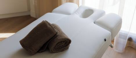 Een massagetafel met handdoeken, een witte hoofdkussen en een houten vloer.