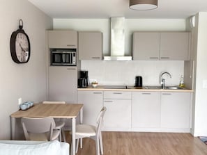 Una cocina moderna con microondas, cafetera y lavabo. Hay una mesa de comedor con sillas y un reloj en la pared.
