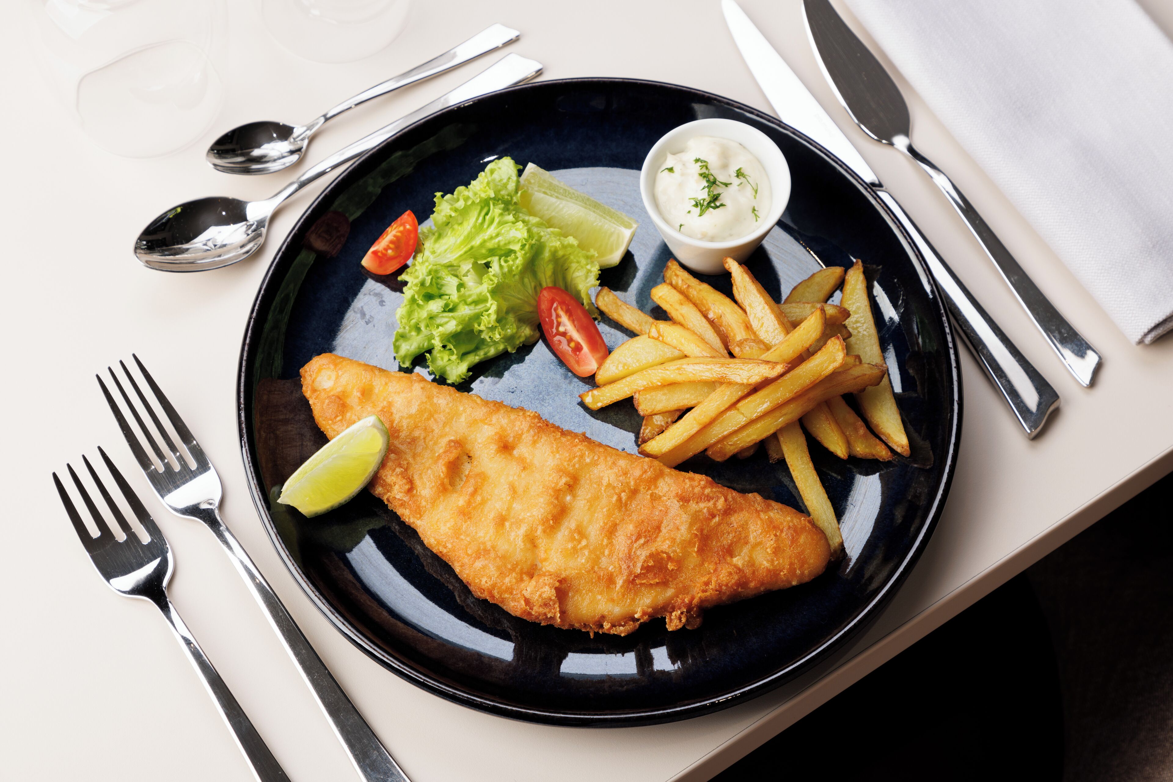 A plate of fish and chips with a side of tartar sauce, lemon, and salad.