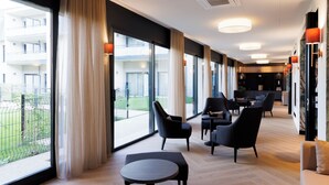 Een moderne hotel lobby met grote ramen, een zithoek met banken en stoelen, en een houten vloer.