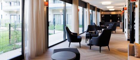 Un moderno vestíbulo de hotel con ventanas amplias, una zona de estar con sofás y sillones, y suelo de madera.