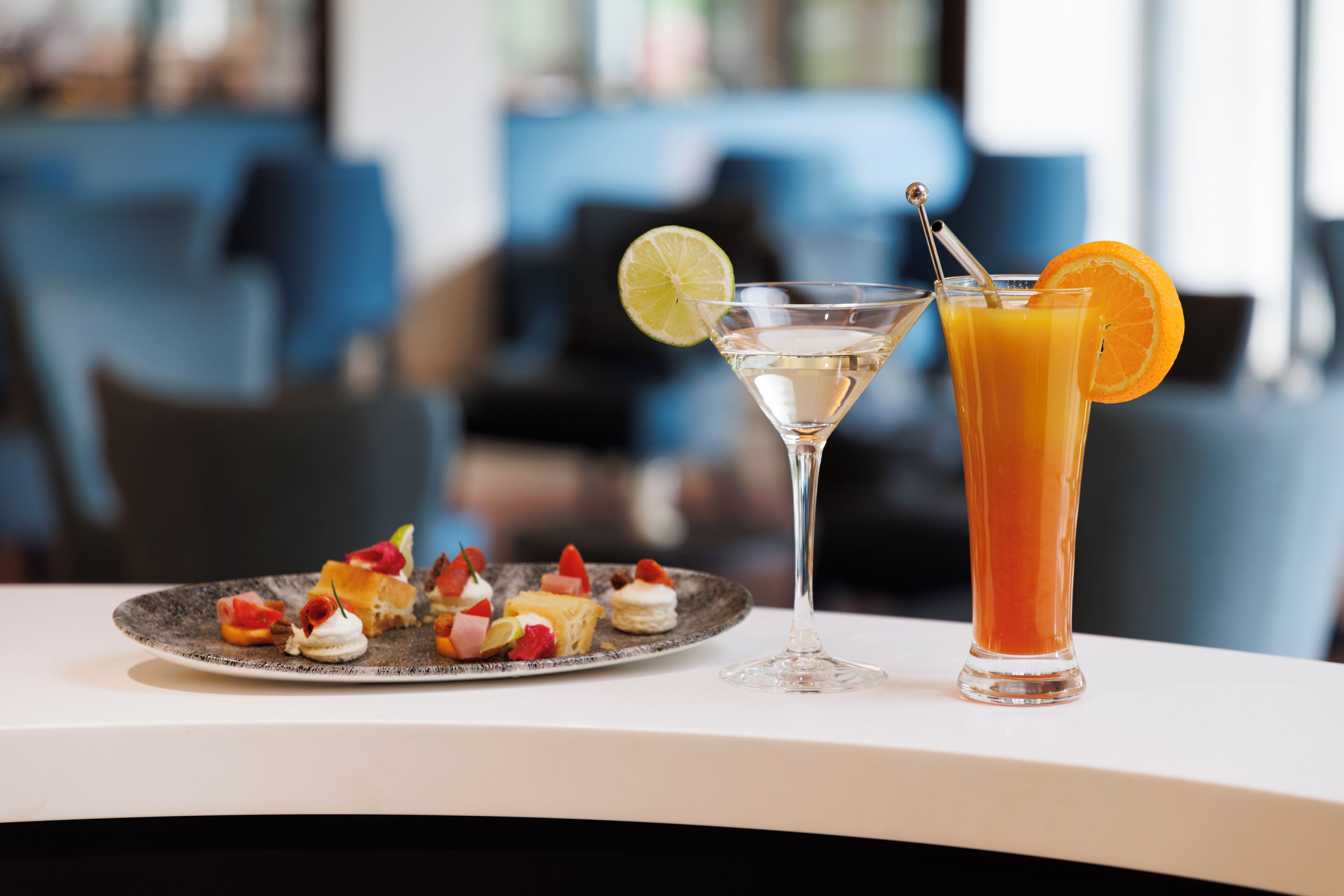 Ein Martini-Glas und ein hohes Glas Orangensaft auf einem Tisch mit einer Platte Vorspeisen.