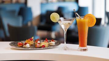 Ein Martini-Glas und ein hohes Glas Orangensaft auf einem Tisch mit einer Platte Vorspeisen.