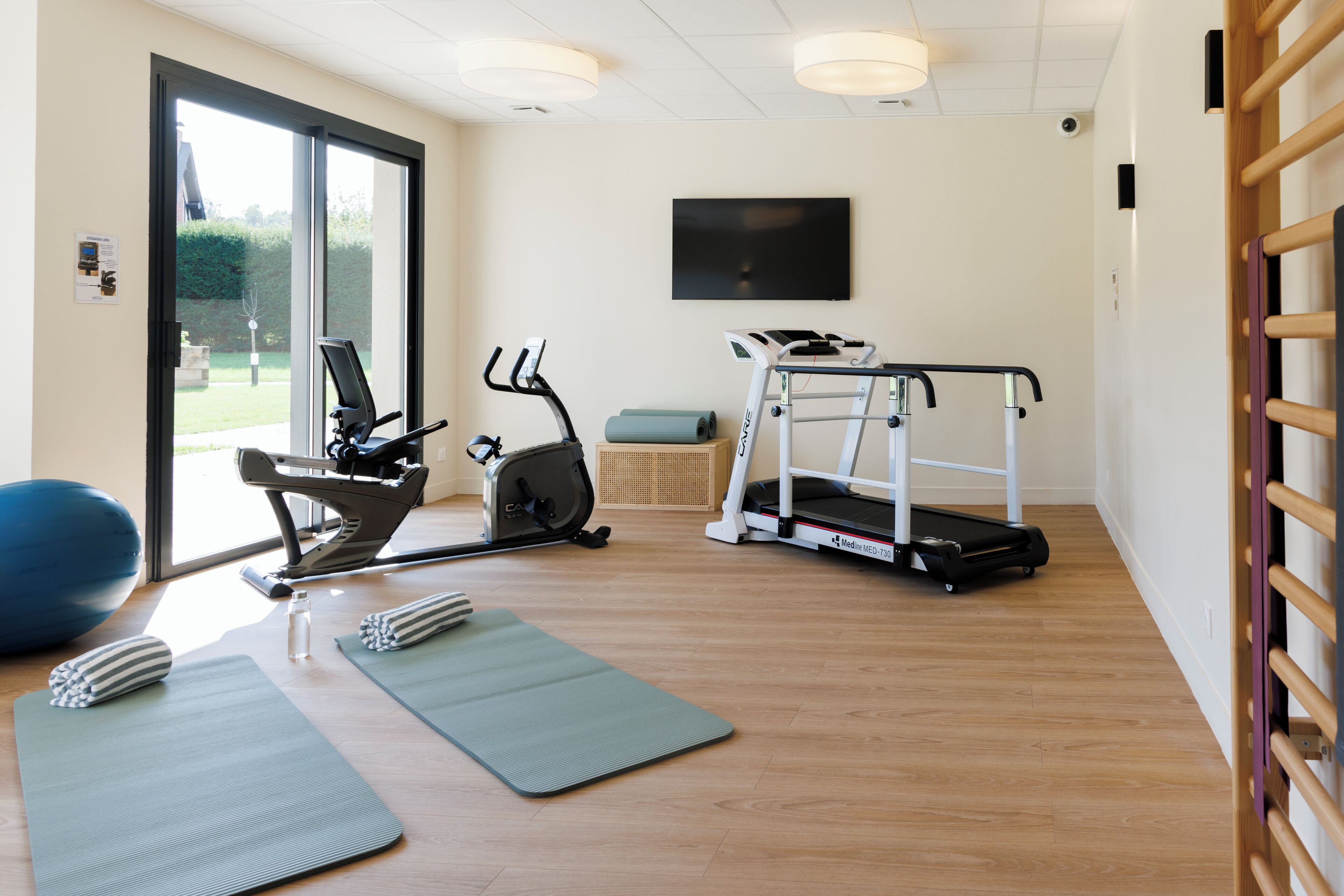 A gym with exercise equipment, yoga mats, and a treadmill.