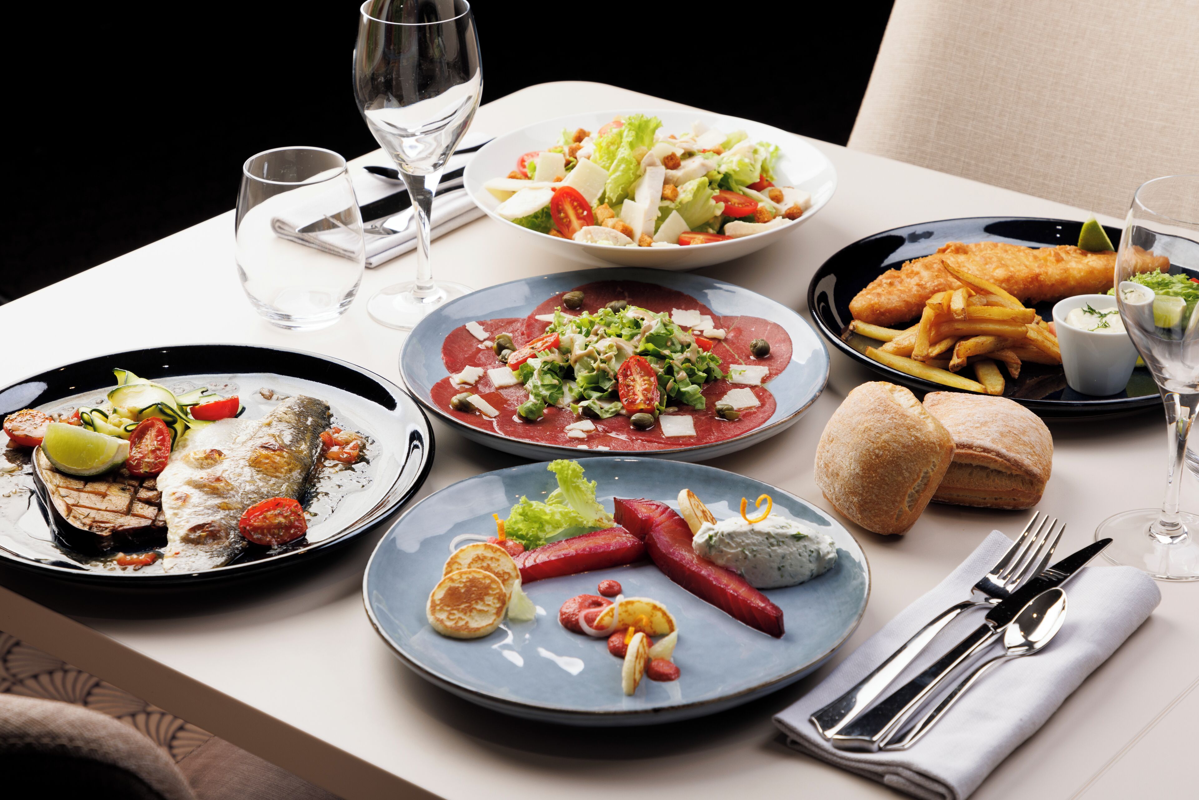 Une table dressée avec divers plats, notamment du poisson, une salade et du pain, ainsi que des verres à vin.