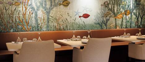 Un restaurante con un mural de una escena submarina, con cabinas y mesas dispuestas para comer.