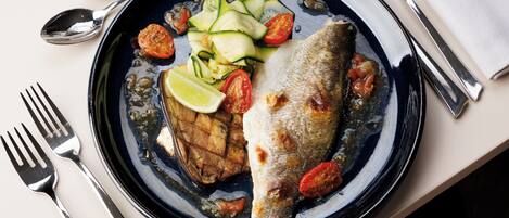 Un plato con pescado a la parrilla, tomates en rodajas y calabacín, acompañado de un gajo de lima.