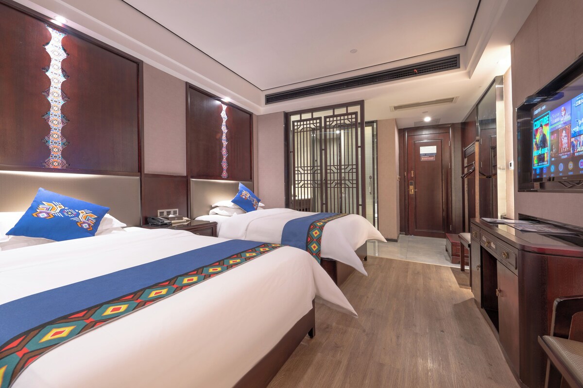Une chambre d’hôtel avec deux lits, un bureau, une télévision et une salle de bain équipée de toilettes et d’une douche.